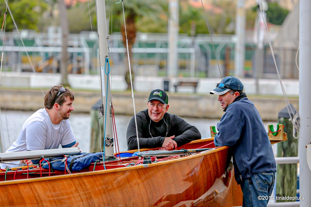 Three sailors around a Thistle sailboat on shore